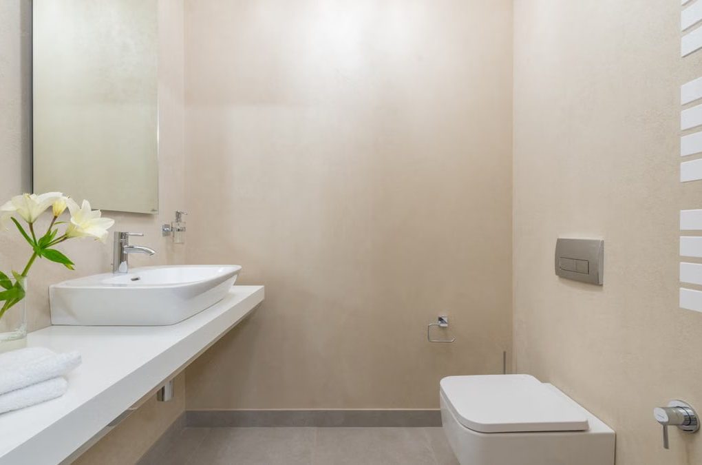 White ceramic toilet placed against wall with mirror and sink near blooming white flowers and towels in light modern bathroom