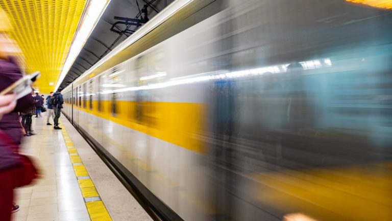 Blurred motion of a train speeding through a vibrant subway platform with commuters.